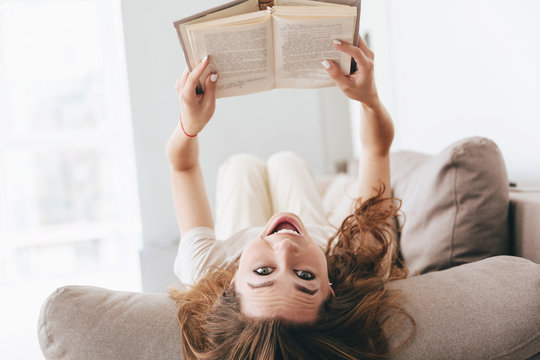 Shot Of Funny Woman Lying On Couch With Book