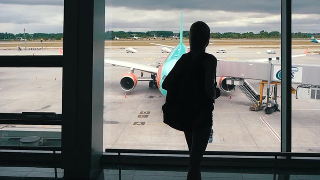 The girl is standing at the window in the airport terminal.