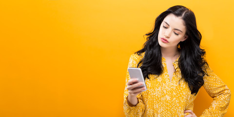 Young woman using her phone on a yellow background