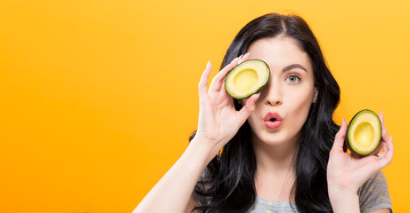 Happy young woman holding avocado halves on a yellow background