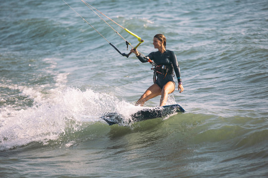 Kite surfing girl in sexy swimsuit with kite in blue sea riding waves with water splash.