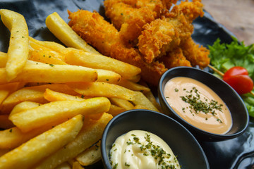 fish and chips with salad cream and wasabi cream sauces in black ceramic dish on wooden table.