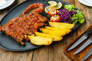 Pork Spare Ribs Barbecue with fried potato and fresh vegetable in black ceramic dish with knife on wooden table