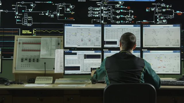 Backside View Operator at Large Control Panel with Screens