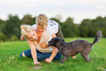 woman romps with her son and a dog on the grass