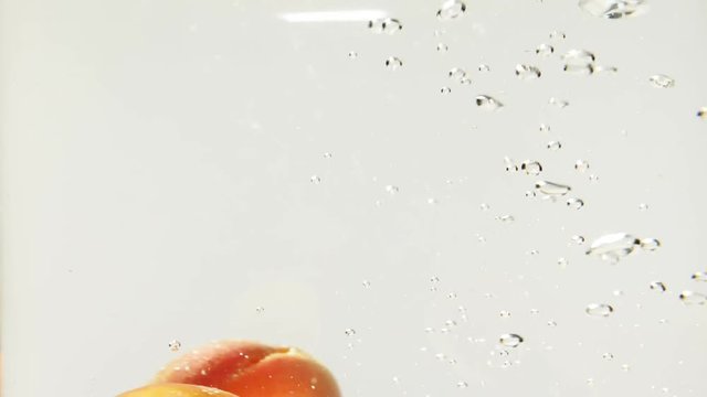 Apricots falling into water in slow motion with a white background