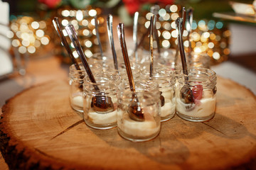 Little bottles with sauces and spoons stand served on wooden dish