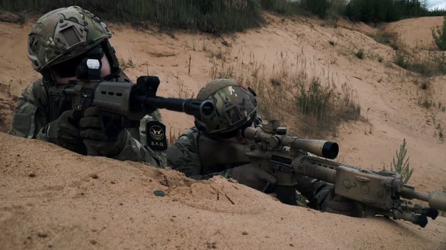 Soldiers with sniper rifle lying on sand front view. Soldiers with weapons