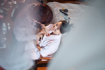 Look from behind the curtains at smiling woman sitting on the chair while artist does her make-up