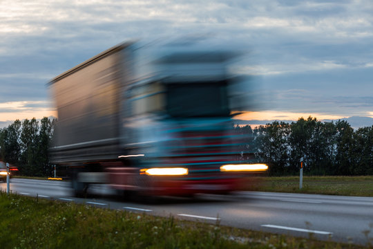 Speeding motion blur oncoming trucks with glowing lights on the highway after sunset. Abstract blur image background with copy space.
