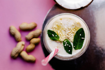 Milk-shake with mint, bananas and sesame stands on table with peanuts