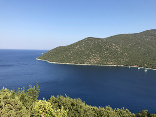 A bay of Kefalonia in Greece, with blue sea and green forest on the mountain.