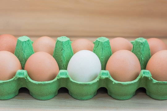 Concept of individuality, exclusivity, better choice. White egg among brown eggs on wooden background.