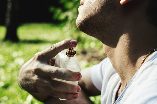 Handsome Young Man Using Perfume On Green Background