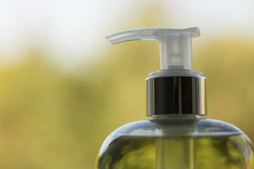 Fototapeta na wymiar Macro: Liquid soap or shampoo in a bottle with a dispenser. This is have a natural green color on a pleasant fuzzy background of leafs. Concept: everyday personal care products.