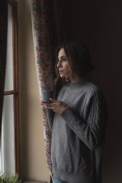 Thoughtful woman having coffee while standing by window