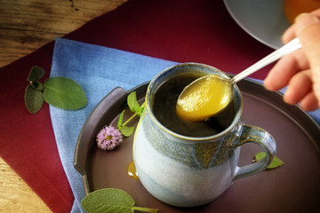 Honey flows from a spoon into a cup of herbal tea with sage and mint against cold or flu,  rustic wood, copy space, selected focus, motion blur and narrow depth of field