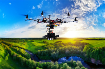 Drone with professional cinema camera flying over a blue calm river in the forests and fields at the sunset.