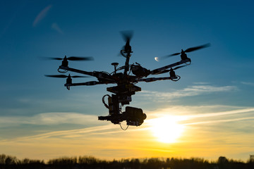 Fototapeta na wymiar Drone with digital camera flying in sky over field on sunset