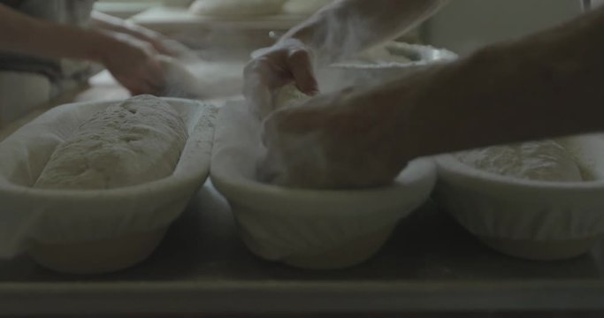 A baker places a loaf of bread dough into a pan for baking later.