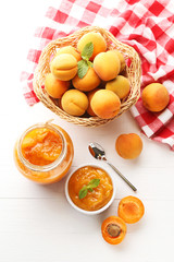 Apricot jam in bowl and glass jar on white wooden table