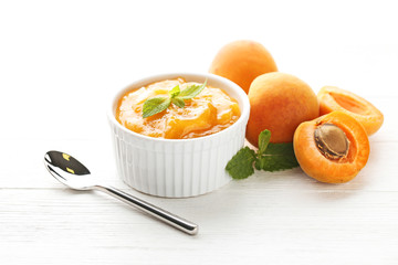 Apricot jam in bowl with spoon on white wooden table