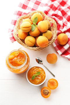 Apricot jam in bowl and glass jar on white wooden table
