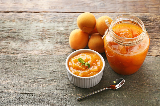 Apricot jam in bowl and glass jar with spoon on grey wooden table