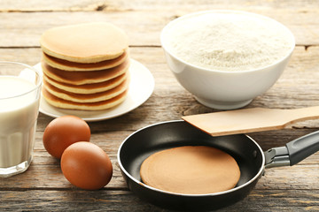 Tasty pancakes with eggs, flour and glass of milk on wooden table