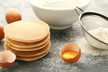 Tasty pancakes with eggs and flour on grey wooden table