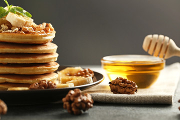 Tasty pancakes with walnuts and bananas on grey wooden plate
