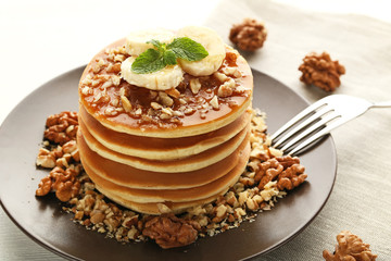 Tasty pancakes with walnuts and bananas on white wooden plate