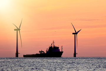 Sustainable resources. Wind farm with ship silhouette at tropical sunrise or sunset. Solar and wind energy and food supply represented.