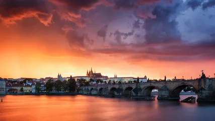 Fototapeten Skyline of Charles bridge and Prague castle on Vltava river during afternoon. Storm clouds with red color. Old Town, Prague, Europe. © daliu