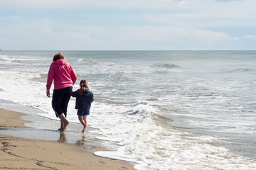 A mother walking wiht her daughter at the beach in a winter day