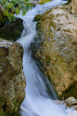 Close up of mossy rock with blurred flowing water rushing downstream