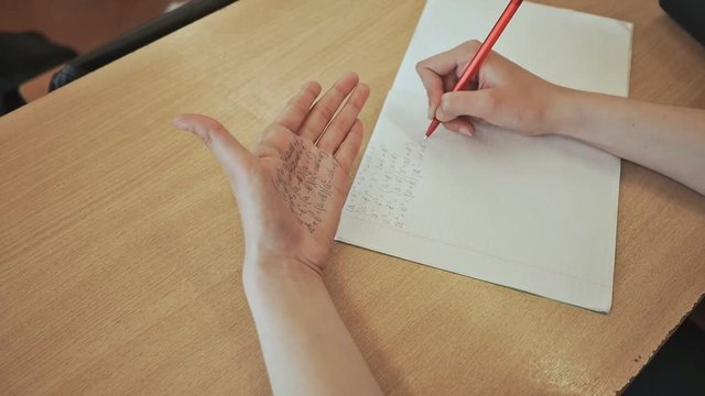 The schoolgirl writes off mathematical formulas from a crib on a hand. School examination.