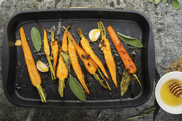 Young juicy carrots baked with honey, sage, garlic, olive oil, salt for a homely comfortable dinner on the background. Top View.