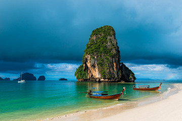 Naklejka premium high rock in the sea, rain cloud and Thai boats near the shore