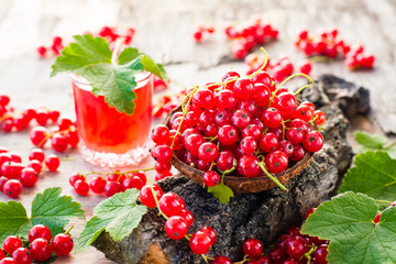 Red currant in a bowl on a tree bark and glass of boiling red currant drink