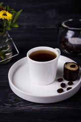 Black coffee in a white cup and chocolate candyon a dark wooden background