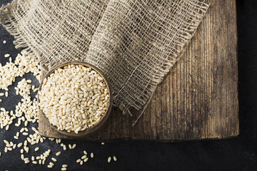 Pearl dry cereal in a vintage wooden bowl on a plain dark background for text placement and advertising. Selective focus.