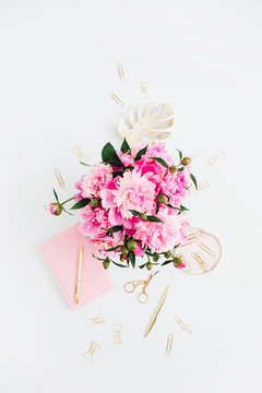 Flat lay home office desk. Female workspace with pink peonies bouquet, golden accessories, pink diary on white background. Top view feminine background.