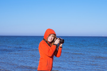 woman tiurist in red jacket with photo camera on the beach, photographer make picture of sea 