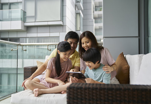 Smiling Family of four bonding on the balcony over an electronic tablet