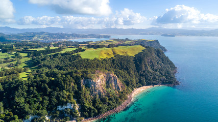 Aerial view on a cliff on a sunny beach with farmland on the background. Coromandel peninsula, New Zealand.