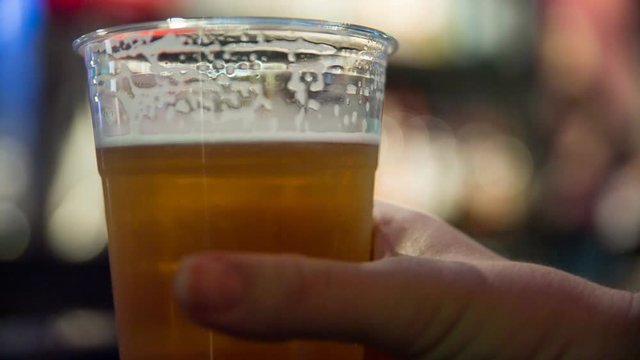 Close Up Tilt to Beer Picked Up in Bar. a hand held tilting shot up a beer in a plastic cup at a bar. Beer is picked up and placed back down
