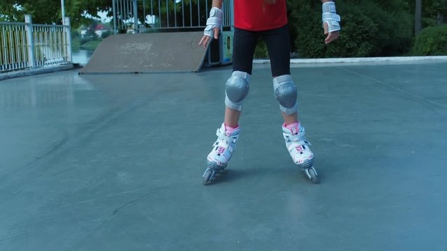 The little girl is learning to skate. The legs of a child in white rollers.