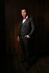 A confident elegant handsome young man standing in front of a wooden background in a studio wearing a nice suit