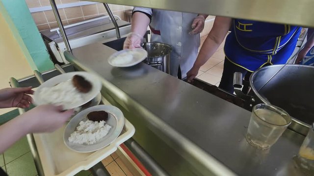 Workers of the school canteen serve schoolchildren by imposing dishes on their plates.